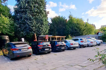 Seven cars parked in a row in an outdoor parking lot with trees and wooden structures behind at Hotel Columbus & Glamping