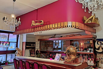 Bar area at Hotel Columbus & Glamping with red chairs, chandelier lighting, wooden shelves and a diving helmet display