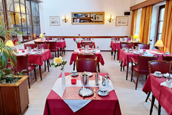 Dining room with red tablecloths and wooden chairs set with tableware and flowers at Hotel Columbus & Glamping