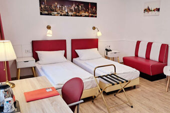 Hotel Columbus & Glamping room with two single beds with red headboards, red and white striped sofa, and wooden floor