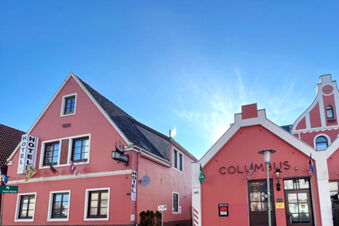 Pink Hotel Columbus & Glamping buildings with flags, windows, and signs under a clear blue sky