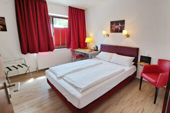 A clean hotel room at Hotel Columbus & Glamping with a double bed, red curtains, a desk with a lamp, and a red armchair