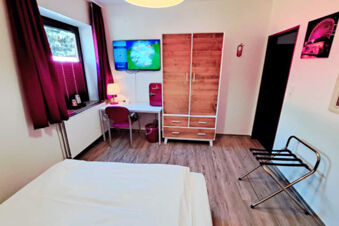 Hotel Columbus & Glamping room with a bed, wooden wardrobe, desk with chair, TV, and purple curtains on the window