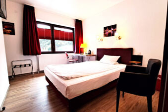 Hotel Columbus & Glamping single room with a bed, desk, chair, window with red curtains, and wooden floor visible