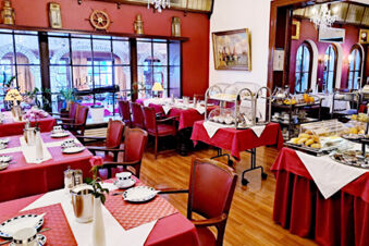 Dining area with tables covered in red and white linens, set with cups and plates, and buffet stations at Hotel Columbus & Glamping