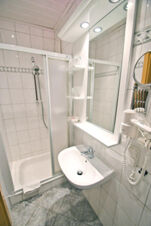 Bathroom with shower cabin, white sink, wall-mounted hairdryer, mirror, shelves, and tiled walls at Rh&ouml;ngasthof Zur Linde & Ferien-Appartements Rh&ouml;nsicht