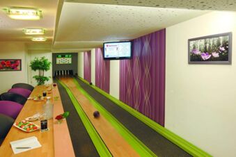 Indoor bowling lane with wooden floor, purple walls, seating area with food and drinks at Rh&ouml;ngasthof Zur Linde & Ferien-Appartements Rh&ouml;nsicht