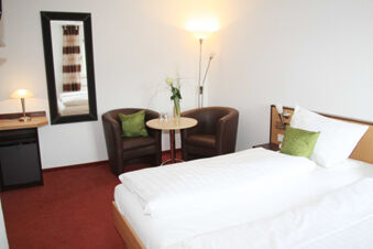 Rh&ouml;ngasthof Zur Linde & Ferien-Appartements Rh&ouml;nsicht hotel room with a bed, two armchairs, table, floor lamp, and wall mirror