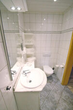 Small bathroom with white tiled walls, a sink with marble countertop, toilet, and neatly folded towels at Rh&ouml;ngasthof Zur Linde & Ferien-Appartements Rh&ouml;nsicht