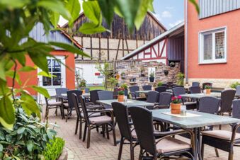 Outdoor seating area with tables, wicker chairs, potted flowers, and a stone wall at Rh&ouml;ngasthof Zur Linde & Ferien-Appartements Rh&ouml;nsicht