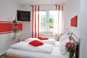 Bright hotel room at Rh&ouml;ngasthof Zur Linde & Ferien-Appartements Rh&ouml;nsicht with two beds, red pillows, and window with striped curtains