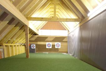 Indoor archery range with three target boards at the end and wooden beams at Rh&ouml;ngasthof Zur Linde & Ferien-Appartements Rh&ouml;nsicht