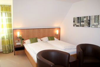 Hotel room at Rh&ouml;ngasthof Zur Linde & Ferien-Appartements Rh&ouml;nsicht with two single beds, green pillows, brown chairs, and wall art