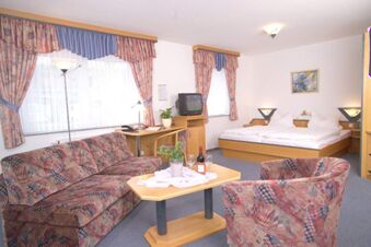 Room interior of Rh&ouml;ngasthof Zur Linde & Ferien-Appartements Rh&ouml;nsicht with patterned sofa and armchair, bed, and wooden furniture