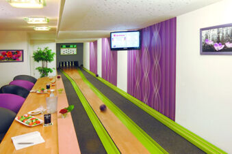 Indoor bowling lane with green gutters, purple patterned walls, dining table with food and drinks at Rh&ouml;ngasthof Zur Linde & Ferien-Appartements Rh&ouml;nsicht