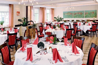 Dining room with round tables set with red napkins and glassware and chairs with red-patterned upholstery at Rh&ouml;ngasthof Zur Linde & Ferien-Appartements Rh&ouml;nsicht