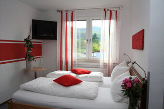 Hotel room with two single beds, white bedding, red pillows, a window with red-striped curtains, and a wall-mounted TV at Rh&ouml;ngasthof Zur Linde & Ferien-Appartements Rh&ouml;nsicht