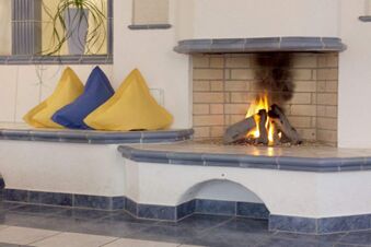corner fireplace with lit fire and a built-in bench with yellow and blue pillows in Rh&ouml;ngasthof Zur Linde & Ferien-Appartements Rh&ouml;nsicht
