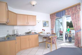 Kitchen area with wooden cabinets, dining table with chairs, and children on the balcony at Rh&ouml;ngasthof Zur Linde & Ferien-Appartements Rh&ouml;nsicht