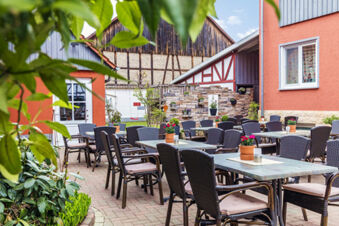 Outdoor patio with black wicker chairs and tables decorated with potted flowers at Rh&ouml;ngasthof Zur Linde & Ferien-Appartements Rh&ouml;nsicht