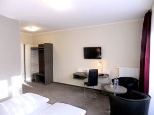 Hell eingerichtetes G&auml;stezimmer mit Doppelbett, Schreibtisch, Flachbild-TV und Sitzecke im K&ouml;hncke's Hotel.