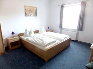 Hell eingerichtetes Schlafzimmer mit zwei Einzelbetten und blauen Nachttischlampen im K&ouml;hncke's Hotel mit Teppichboden.
