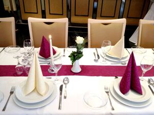 Eleganter festlich gedeckter Esstisch mit wei&szlig;en und violetten Servietten, Kerze und Rosenvase im Restaurant von K&ouml;hncke's Hotel.