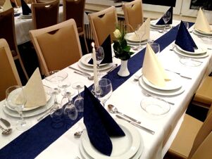 Eleganter eingedeckter Tisch mit wei&szlig;er Tischdecke, blauen und cremefarbenen Servietten und Kerze im K&ouml;hncke's Hotel Restaurant.