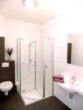 Modernes, sauberes Badezimmer mit Dusche, WC und Waschbecken in K&ouml;hncke's Hotel, ausgestattet mit wei&szlig;en Fliesen und Handt&uuml;chern.