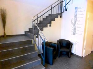 Moderner Eingangsbereich mit Treppe und zwei schwarzen Sesseln im Lobbybereich von K&ouml;hncke's Hotel, begr&uuml;&szlig;t G&auml;ste freundlich.