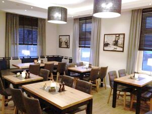 Gem&uuml;tlicher Speiseraum mit Holztischen und St&uuml;hlen bei K&ouml;hncke's Hotel, dekoriert mit Kerzen und Bildern an den W&auml;nden.
