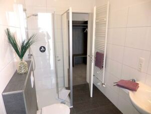 Modernes Badezimmer mit Dusche, Toilette und Waschbecken im K&ouml;hncke's Hotel, hell und sauber mit Fliesen und Handt&uuml;chern.