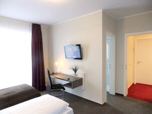Helles und modern eingerichtetes Hotelzimmer mit Schreibtisch und Fernseher im K&ouml;hncke's Hotel mit Blick auf Flur und Bad.