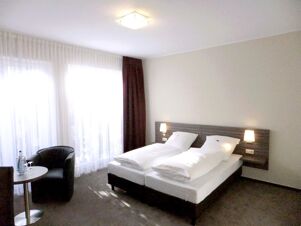 Helles Hotelzimmer mit zwei Einzelbetten, Nachttischlampen und Sitzbereich mit Tisch und Stuhl im K&ouml;hncke's Hotel.
