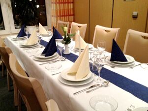 Eleganter gedeckter Tisch mit wei&szlig;en und blauen Servietten in einem Speiseraum von K&ouml;hncke's Hotel bei ged&auml;mpftem Licht.