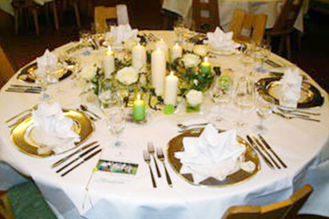 Round table set with white tablecloth, folded napkins, golden chargers, candles, and glassware at Hotel Gasthaus Hirschen