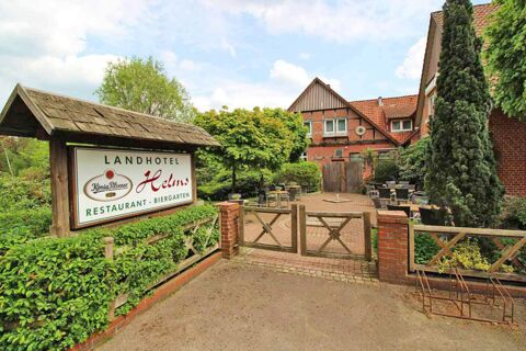 Au&szlig;enansicht des Landhotel Helms mit einem Biergarten, Sitzgelegenheiten und gr&uuml;ner Umgebung an einem sonnigen Tag.