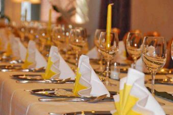 Festlich gedeckter Tisch im Landhotel Helms mit wei&szlig;-gelben Servietten, Kerzen und Gl&auml;sern f&uuml;r ein elegantes Abendessen.