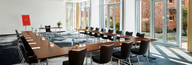 Moderner Konferenzraum mit U-f&ouml;rmig angeordneten Tischen, St&uuml;hlen und Wasserflaschen im NH Collection Hotel Heidelberg mit gro&szlig;en Fenstern.