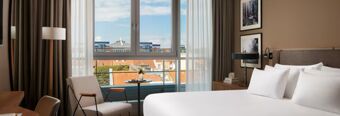 Helles und modernes Hotelzimmer mit gro&szlig;em Bett und Balkon, mit Blick auf die Stadt im NH Collection Hotel Heidelberg.