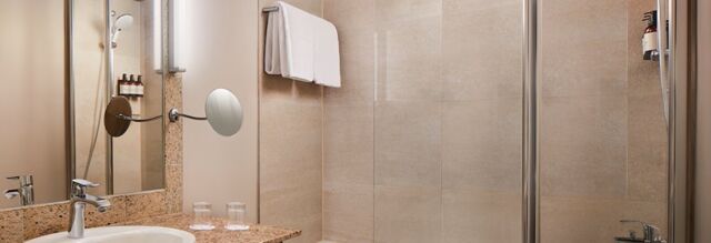Modernes Badezimmer mit Dusche, Handt&uuml;chern und Waschbecken im NH Collection Hotel Heidelberg, elegant und einladend gestaltet.