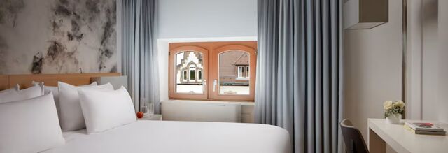 Modern eingerichtetes Hotelzimmer mit wei&szlig;er Bettw&auml;sche und Fenster mit Blick auf historische Geb&auml;ude im NH Collection Hotel Heidelberg.