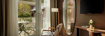 Helles, modern eingerichtetes Zimmer im NH Collection Hotel Heidelberg mit Balkon, gem&uuml;tlichem Sessel und Blick auf begr&uuml;nten Innenhof.