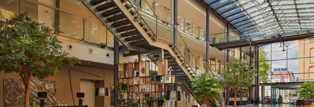 Heller und moderner Lobbybereich mit gro&szlig;er Glasdecke, Pflanzen und offener Treppe im NH Collection Hotel Heidelberg.