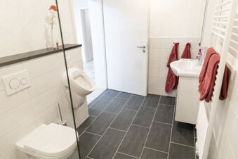 Modernes Badezimmer mit wei&szlig;er Ausstattung, roten Handt&uuml;chern und einer sauberen Optik im Ferienhof Klaucke.