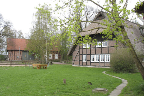 Traditionelle Fachwerkh&auml;user mit Reetd&auml;chern und Gr&uuml;nfl&auml;che im Au&szlig;enbereich des Ferienhof Klaucke bei bew&ouml;lktem Himmel.