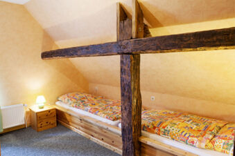 Gem&uuml;tliches Schlafzimmer mit Dachschr&auml;ge und Holzbalken im Ferienhof Klaucke, ausgestattet mit zwei Betten und einem Nachttisch mit Lampe.