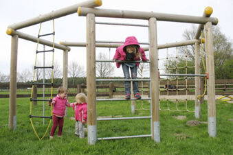 Kinder spielen auf einem Kletterger&uuml;st im Au&szlig;enbereich des Ferienhof Klaucke mit gr&uuml;nem Gras und l&auml;ndlicher Umgebung im Hintergrund.