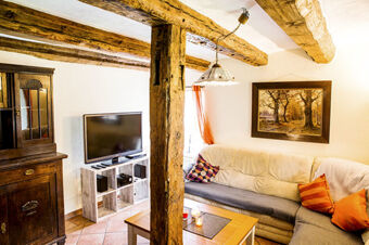 Gem&uuml;tlicher Wohnbereich mit Holzbalken, Fernseher und Sofa im Ferienhof Klaucke, ideal zum Entspannen nach einem Tag im Freien.