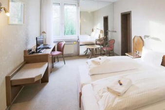 Hell eingerichtetes Hotelzimmer mit zwei Einzelbetten, Schreibtisch, St&uuml;hlen und gro&szlig;em Fenster im Hotel Kick.